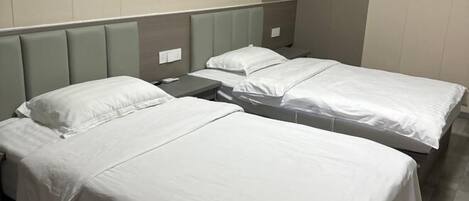 A hotel room with two single beds, each with a grey headboard and white bedding.