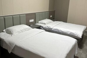 Une chambre d’hôtel avec deux lits simples, chacun doté d’une tête de lit grise et de linge de lit blanc.