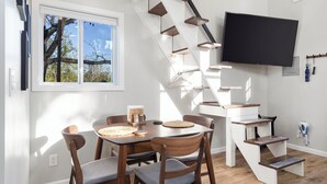 A modern kitchen with a dining table, chairs, a staircase, and a TV mounted on the wall.