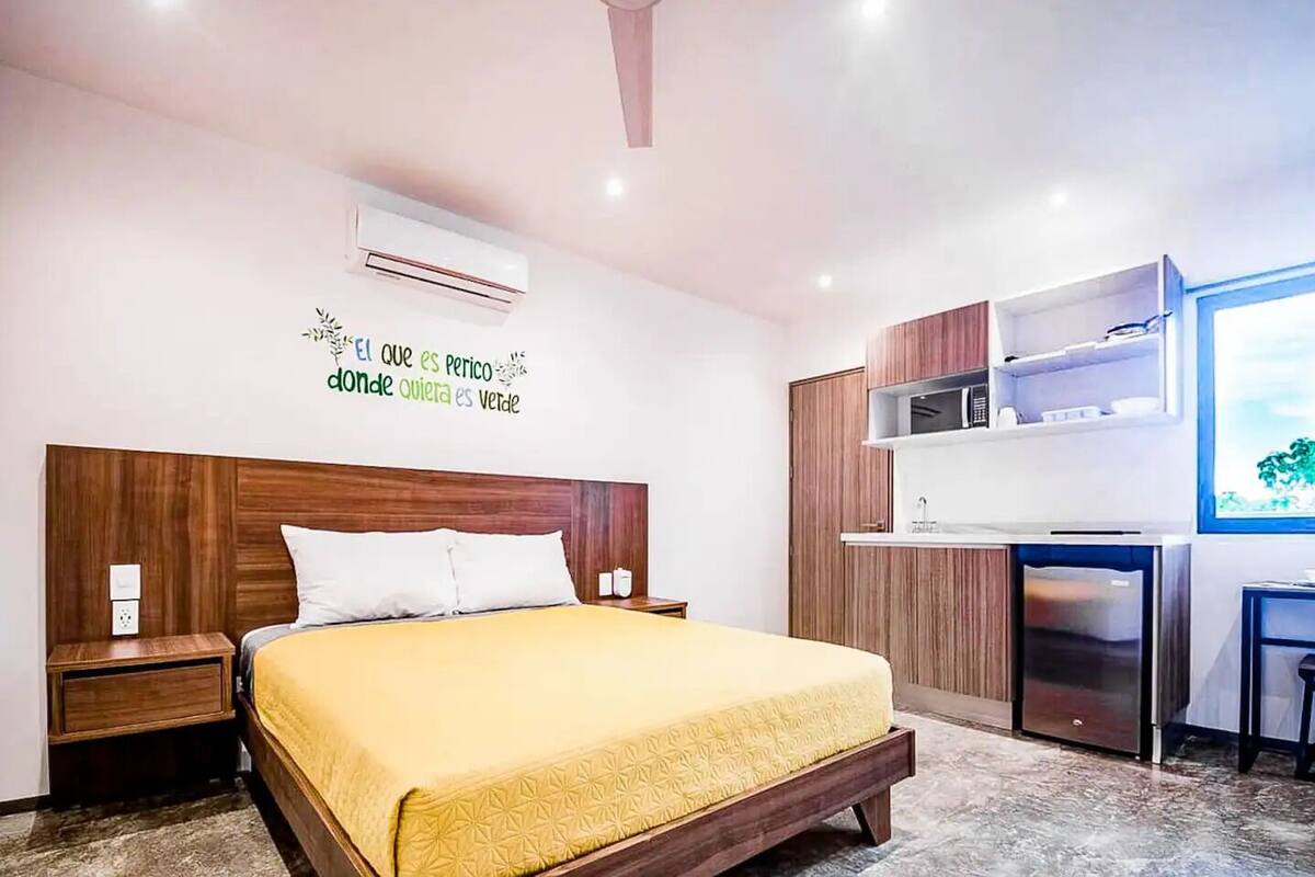 A modern bedroom with a wooden bed, a built-in wardrobe, a small kitchenette, and a wall-mounted air conditioner.
