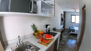 A modern kitchen with a microwave, sink, and a fruit bowl containing pineapple, banana, and watermelon. - El Mexicano (Playa del Carmen)