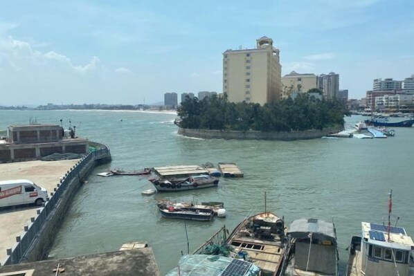 A waterfront area with a prominent building, boats docked along the shore, and a bridge connecting to the land.