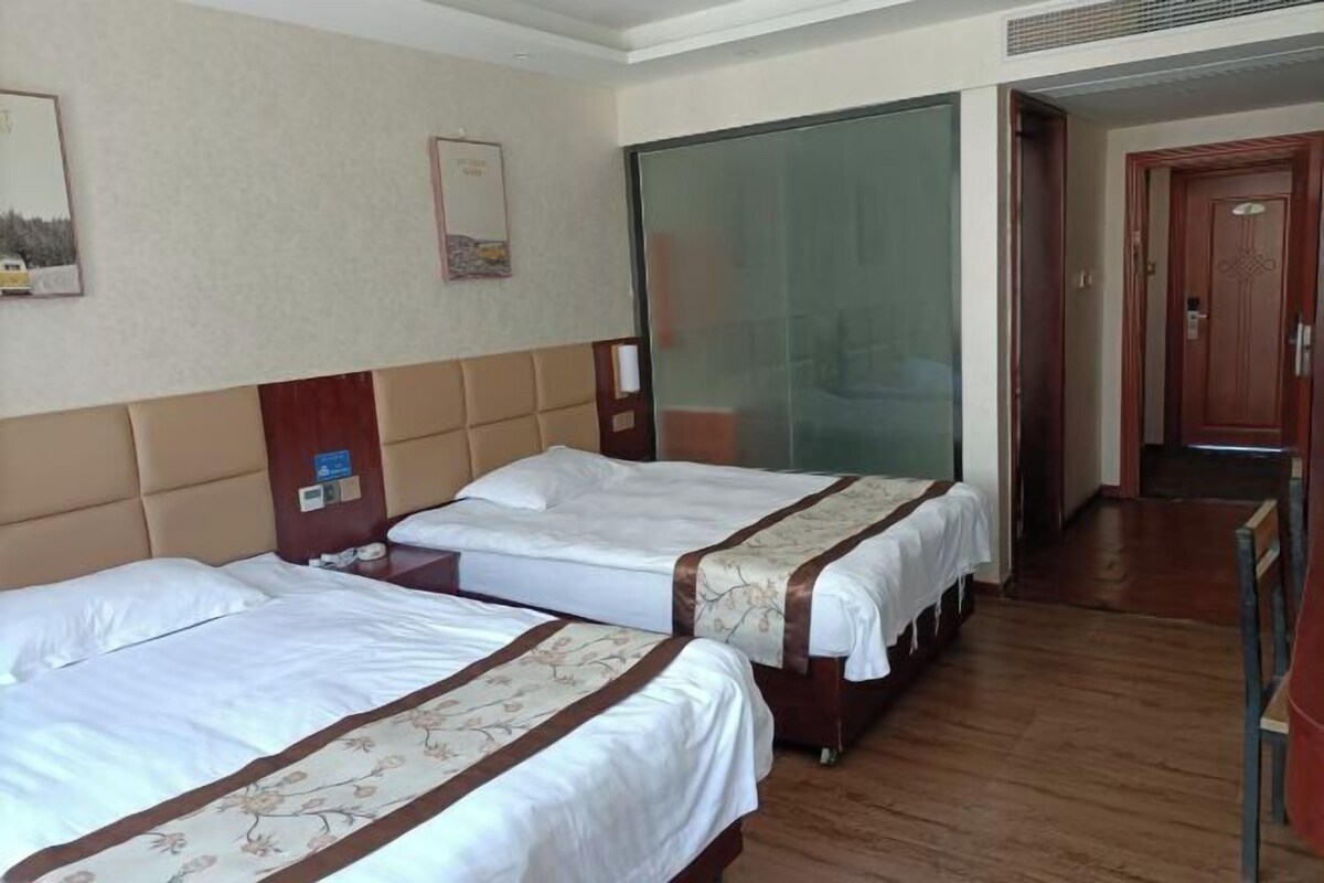 A hotel room with two beds, wooden flooring, a large mirror, and a door leading to another room.