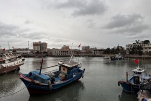 A harbor with several boats docked, buildings in the background, and a cloudy sky.