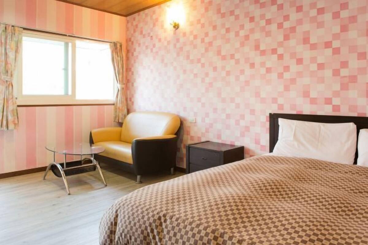 A hotel room with a bed, a small table, a chair, and a nightstand.