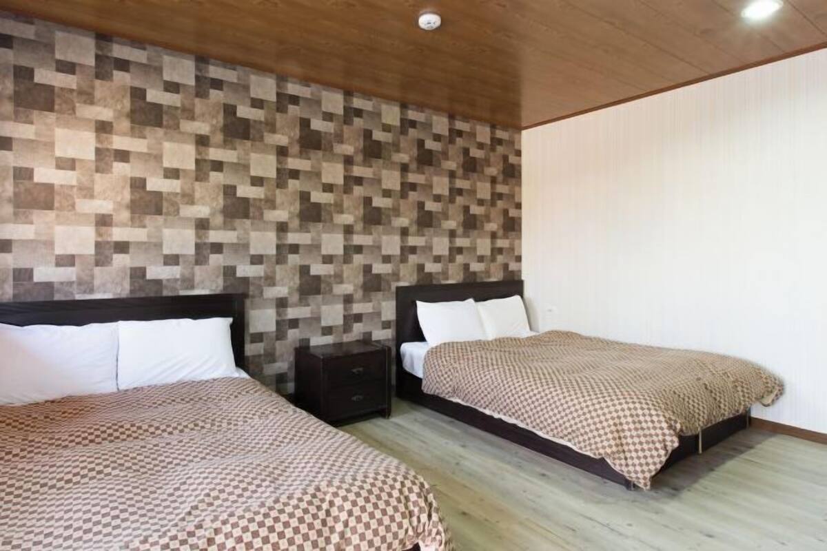 A hotel room with two beds, wooden flooring, a checkered bedspread, and a wall with a pixelated pattern.
