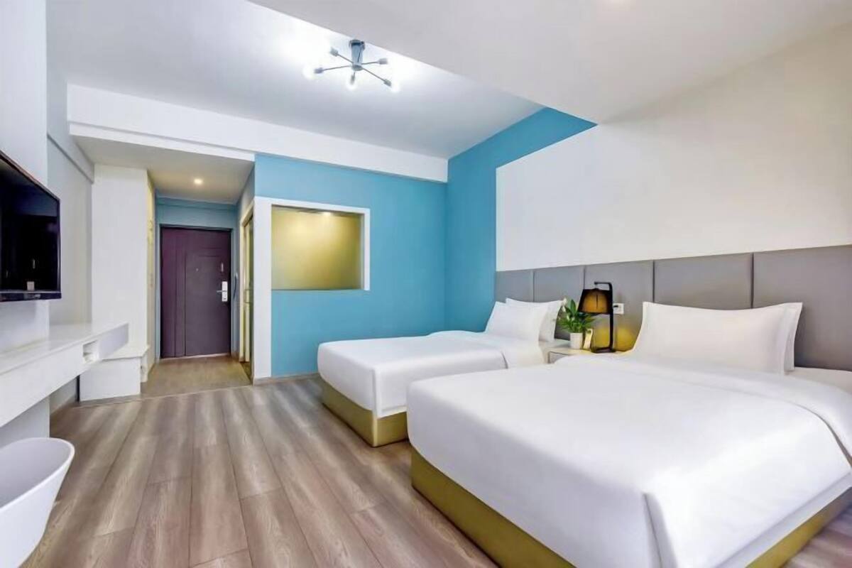 A hotel room with a large bed, two smaller beds, a TV, a desk, and a bathroom.