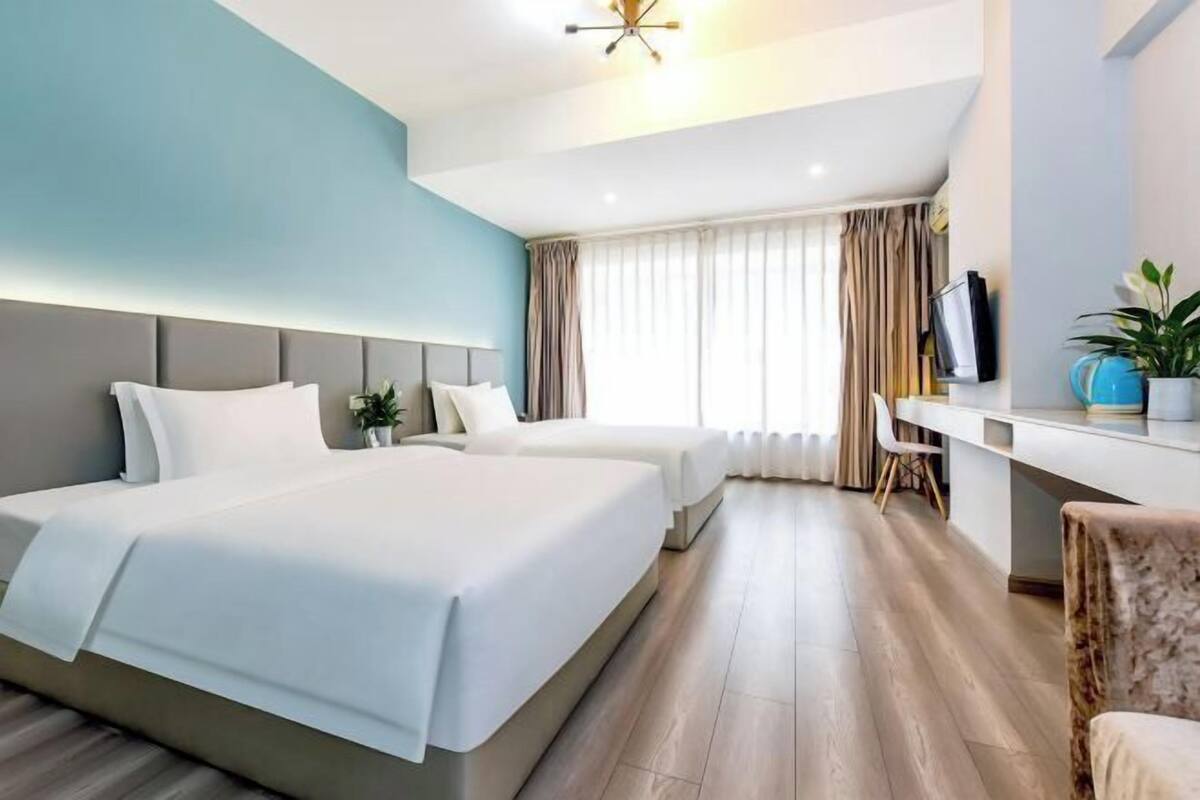 A hotel room with two beds, a desk, a chair, and a television.