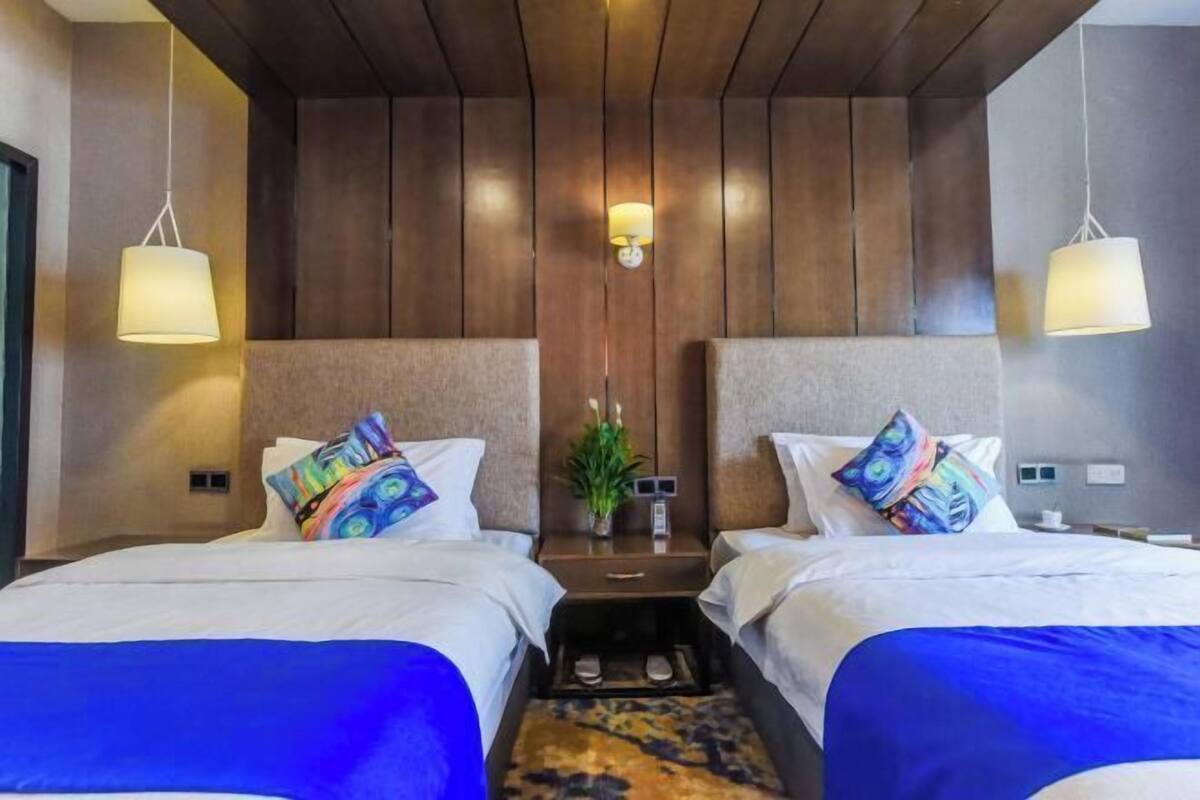 A hotel room with two beds, a small table, and a wall-mounted lamp.