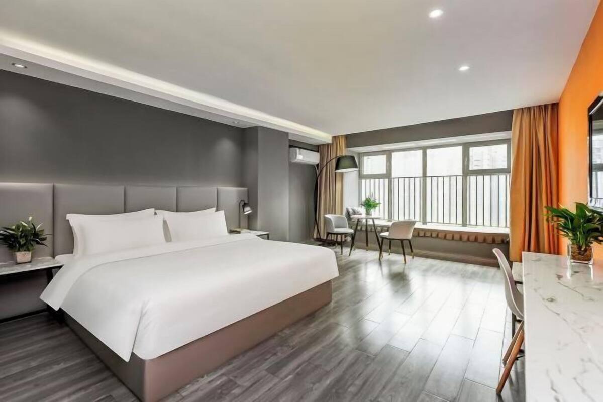 A modern hotel room with a large bed, a desk, and a window with curtains.