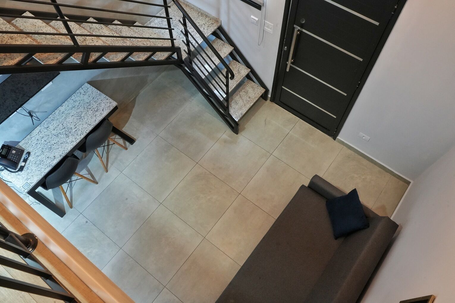 A modern kitchen with a granite countertop, a dining table with chairs, a staircase with a metal railing, and a dark door.
