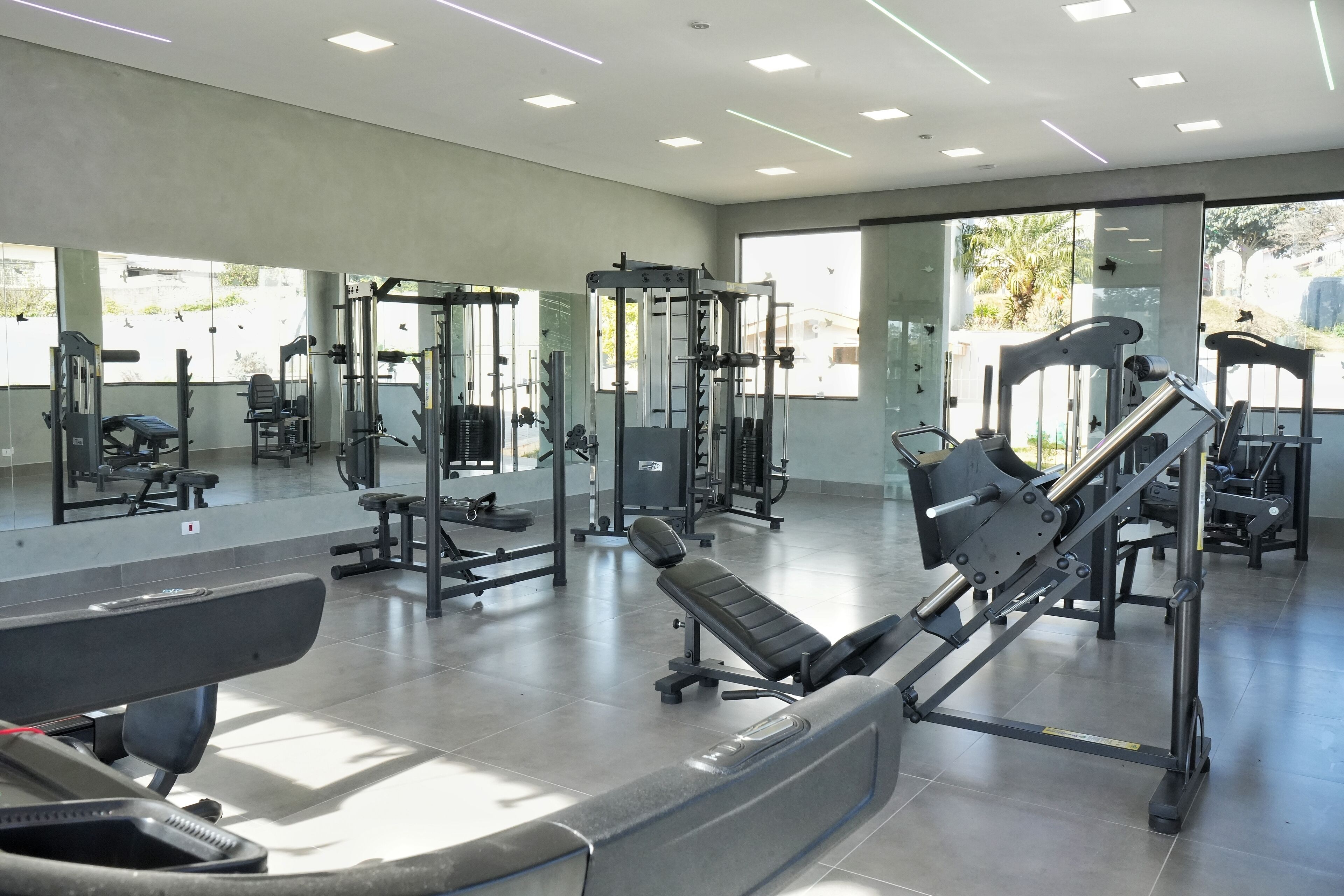 A modern gym with various exercise equipment, large mirrors, and a spacious layout.
