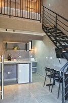 Cozinha moderna com ilha central, área de jantar com cadeiras e escada que leva a um andar superior.