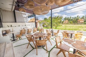 An outdoor seating area with wicker tables and chairs, a covered section with a ceiling fan, and a view of a green landscape. - Tamantara Suites & Villa (Bali)
