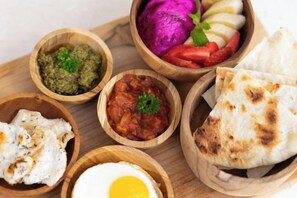 A wooden tray with various food items including flatbreads, a boiled egg, and a bowl of sauce. - Tamantara Suites & Villa (Bali)