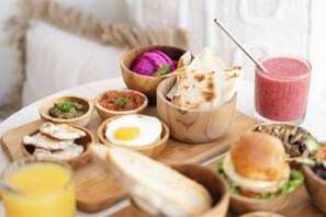 A wooden board with various food items including a burger, a fried egg, and a smoothie. - Tamantara Suites & Villa (Bali)