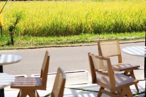 Outdoor seating with tables and chairs, a road, and a field of crops. - Tamantara Suites & Villa (Bali)