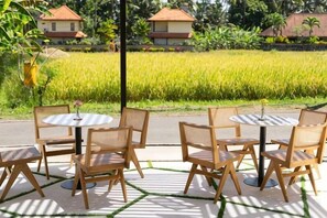 Outdoor seating with tables and chairs, a view of a rice field, and houses in the background. - Tamantara Suites & Villa (Bali)