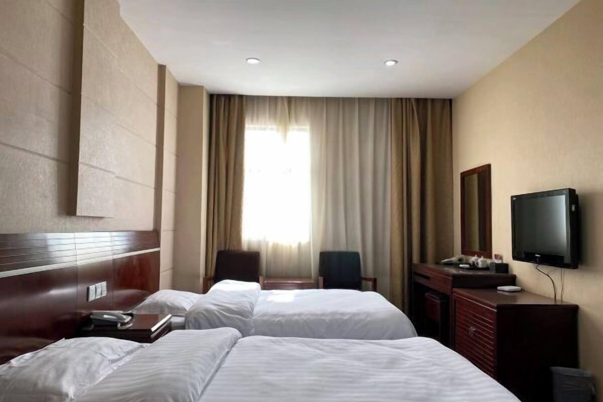 A hotel room with two beds, a television, a desk, and a window with curtains.