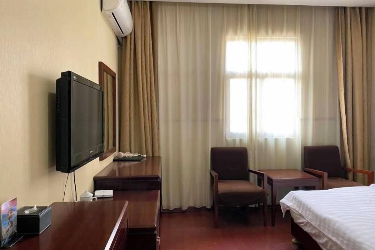 A hotel room with a bed, a desk with a television, two chairs, and a window with curtains.