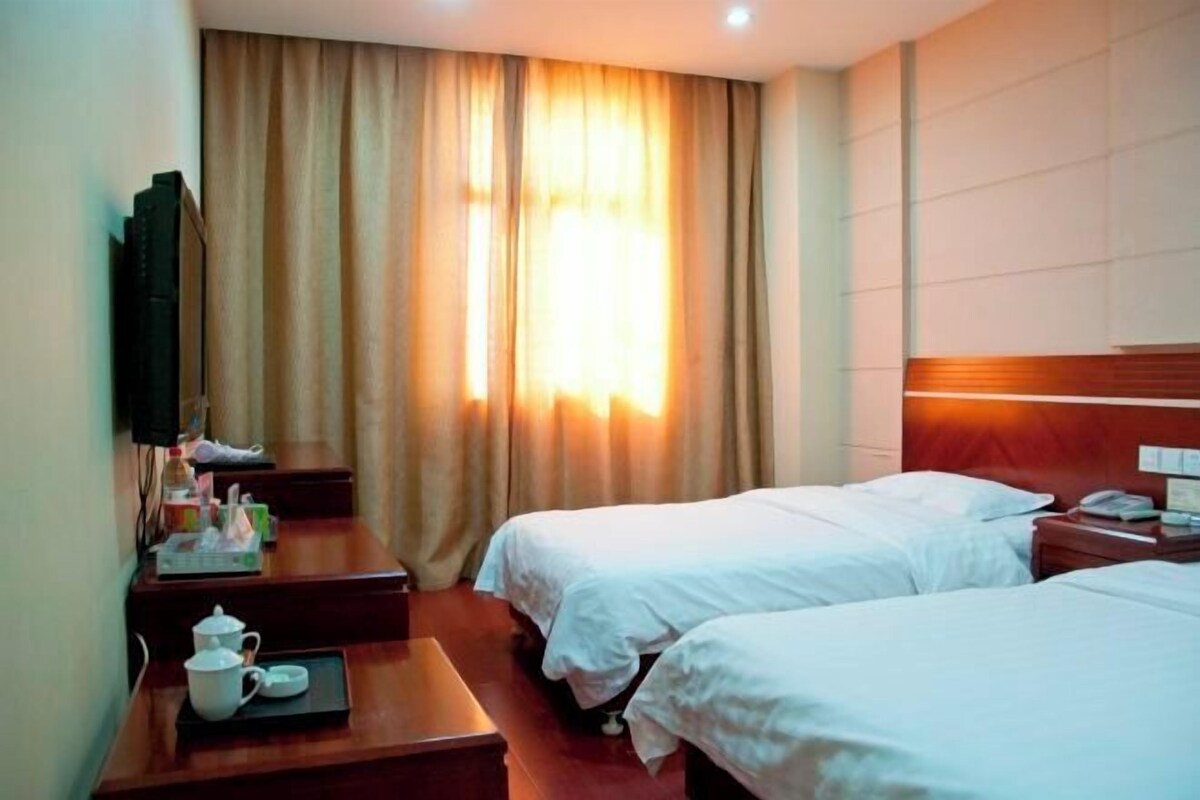 A hotel room with two beds, a TV, a desk with a telephone, and a window with curtains.