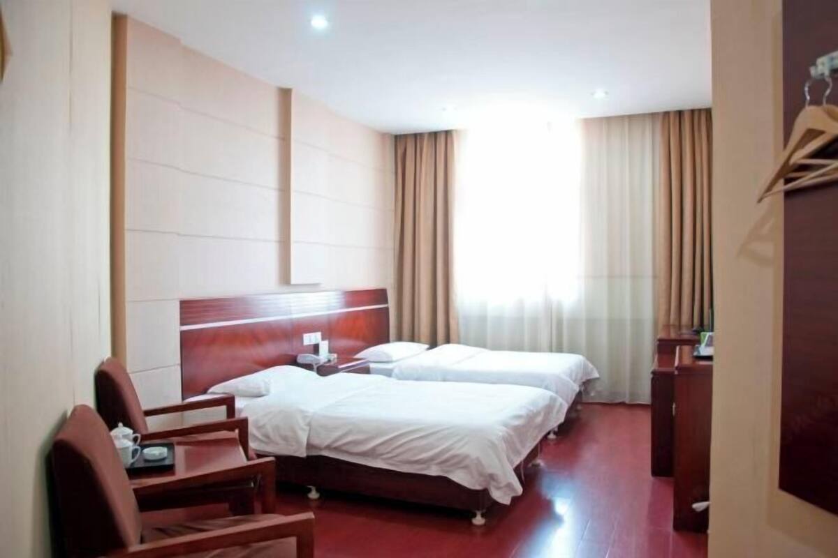 A hotel room with two beds, a wooden headboard, a desk with a chair, and a window with curtains.