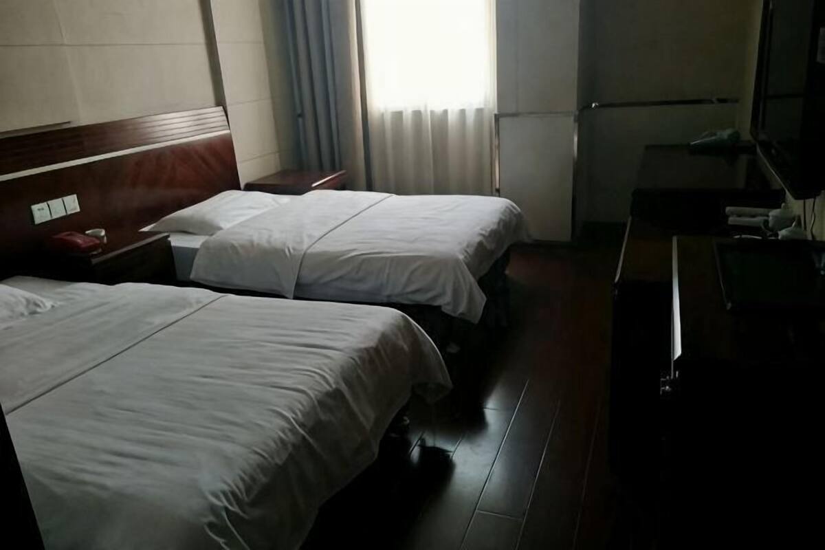 A hotel room with two beds, a wooden headboard, a desk, and a window with curtains.