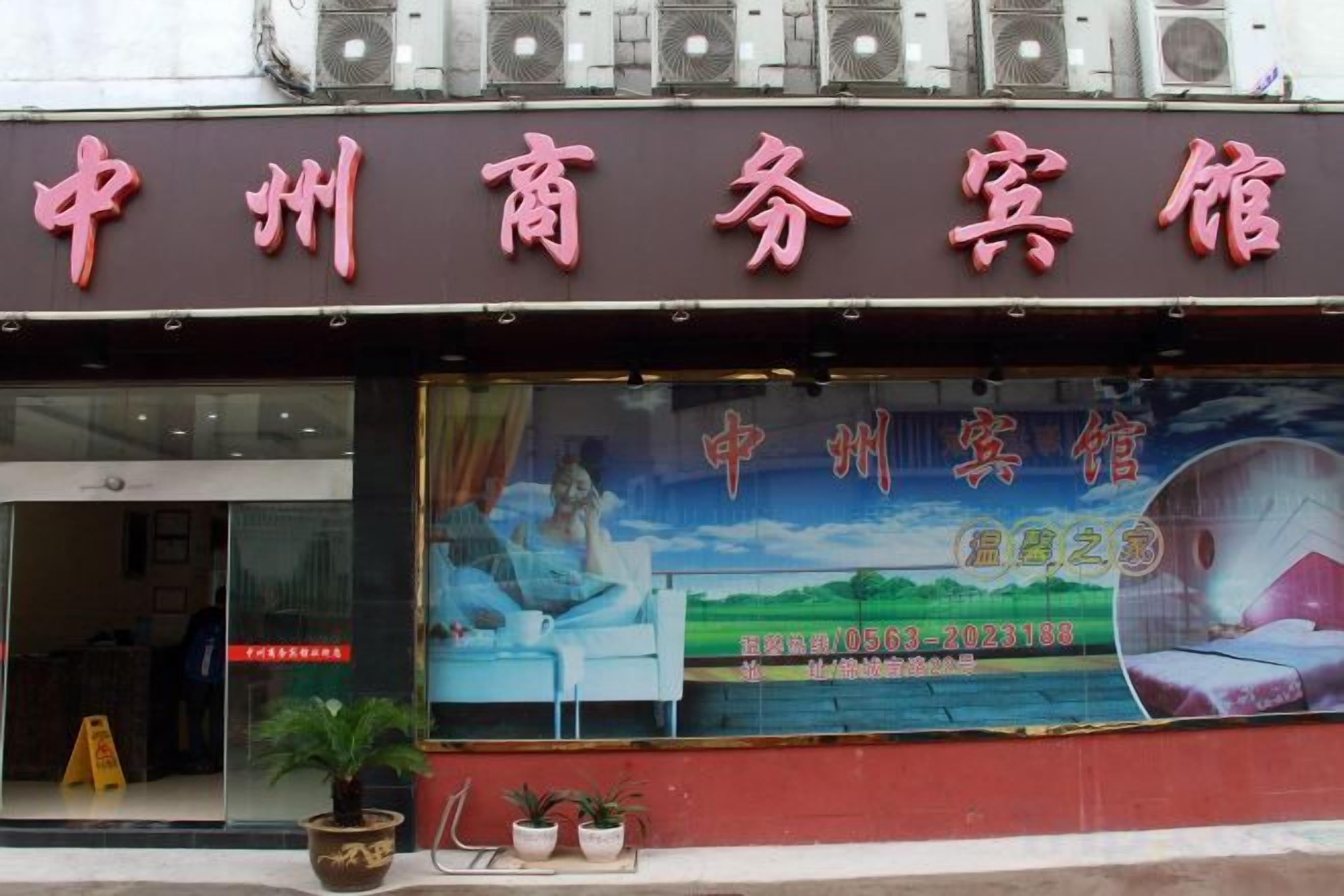 A hotel with a large signboard, a window with a landscape view, and a few potted plants outside.