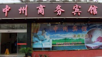 A hotel with a large signboard, a window with a landscape view, and a few potted plants outside.