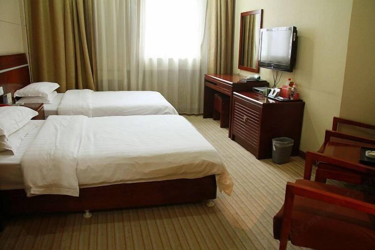 A hotel room with two beds, a desk, a television, and a waste bin.