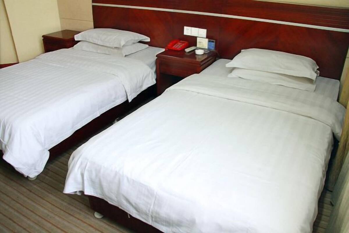 Two single beds with white linens, wooden headboards, and bedside tables with a red telephone.