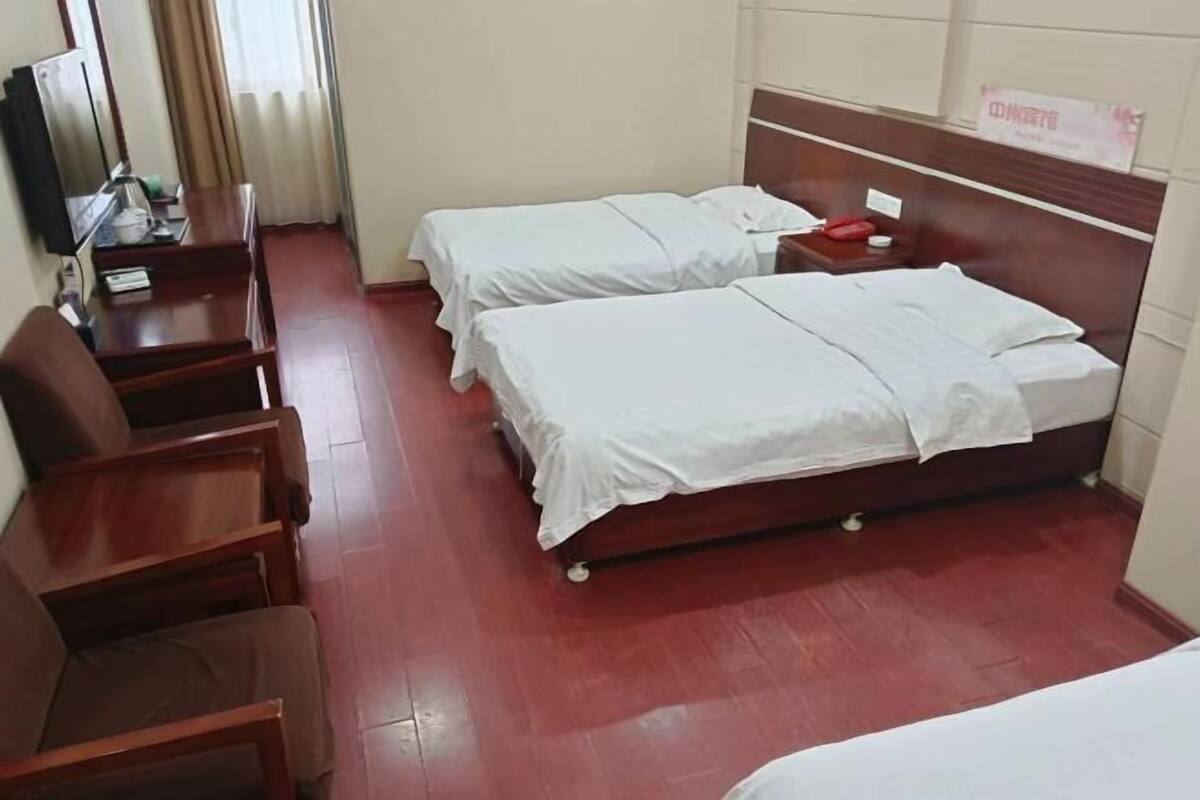A hotel room with two single beds, a wooden desk with a chair, a television, and a sign on the wall.