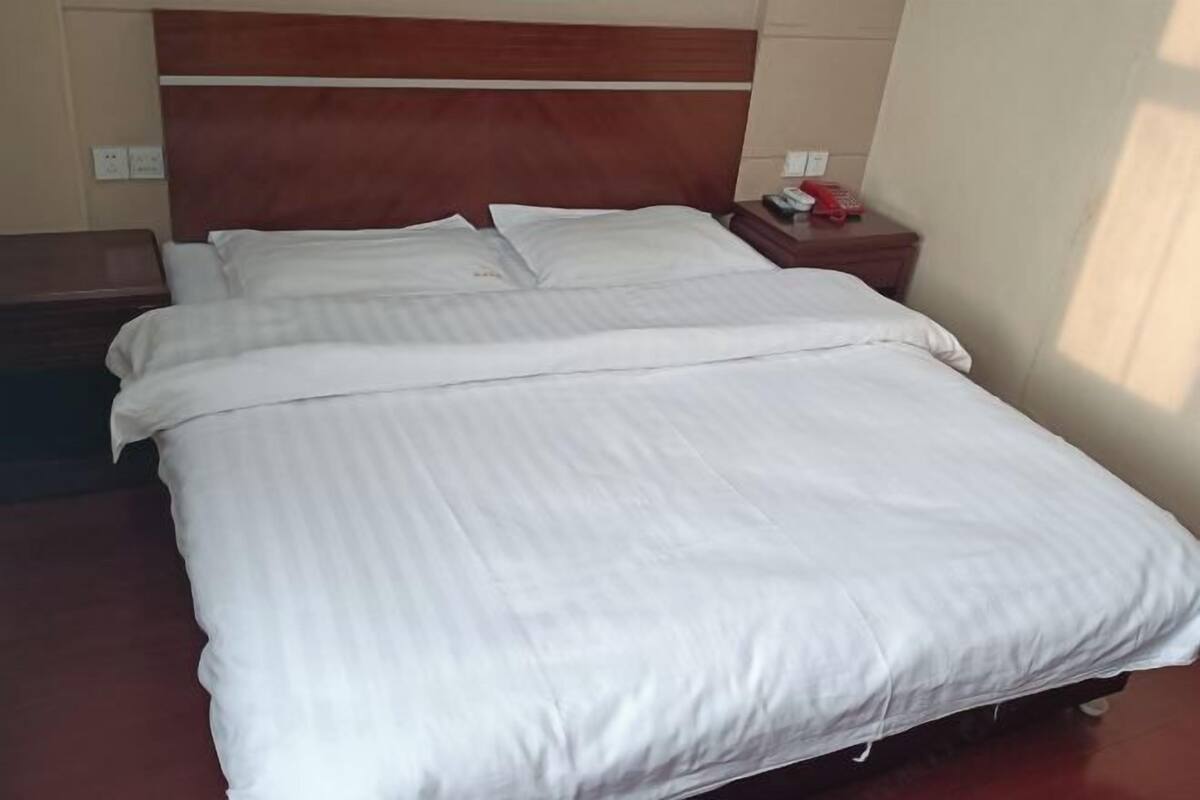 A neatly made bed with white linens, a wooden headboard, and a bedside table with a red telephone and a small item on it.