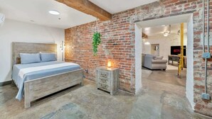 A bedroom with a wooden bed, a nightstand, a brick wall, and a hanging plant.