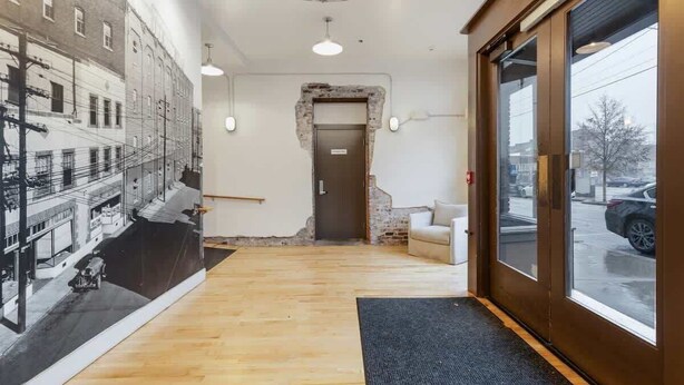 A hotel lobby with a large mural, a wooden floor, a reception desk, and a large window with a view of the street.