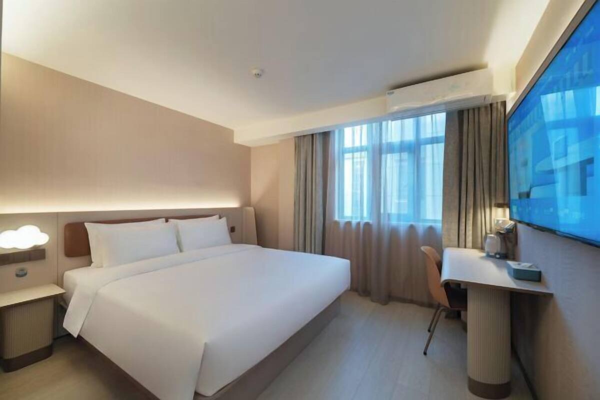 A hotel room with a large bed, a desk, a chair, and a TV on the wall.