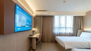 A hotel room with a bed, a desk, a chair, a TV mounted on the wall, and a window with curtains.
