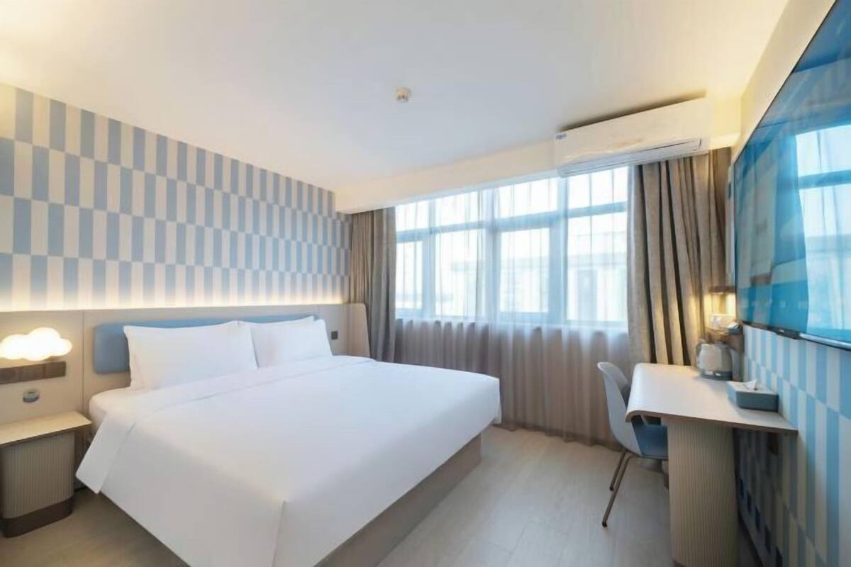 A hotel room with a large bed, a desk, and a window with curtains.