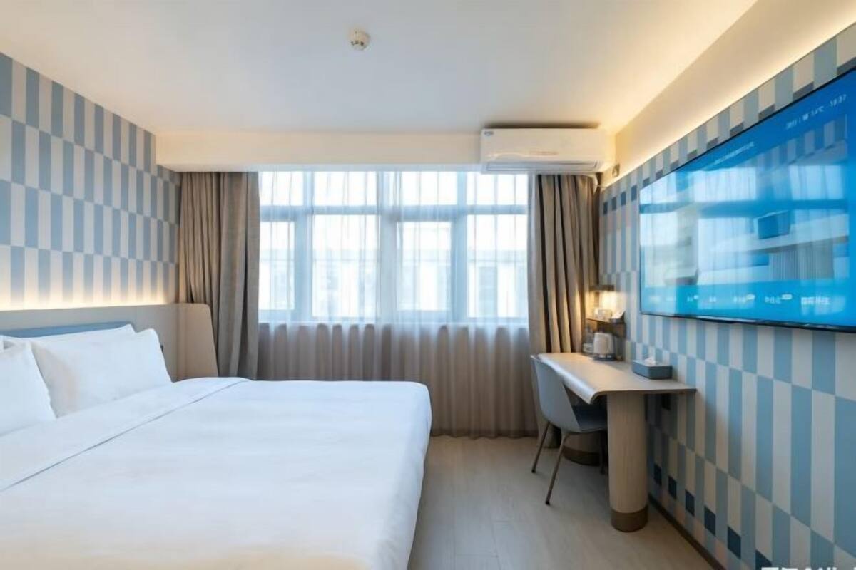 A hotel room with a bed, a desk, a flat-screen TV, and a window with curtains.