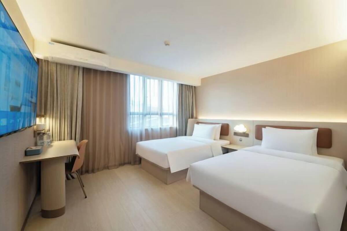 A hotel room with two beds, a desk, a chair, and a TV.