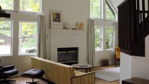 Un salon spacieux doté d’une cheminée, de grandes fenêtres et d’un ventilateur de plafond.