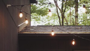 Une terrasse en bois avec une porte vitrée donnant sur une pièce, des guirlandes lumineuses et des plantes en pot.