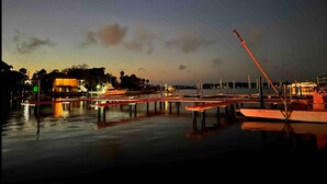 Ein Yachthafen im Abendlicht mit vertäuten Booten, einem Kran und Gebäuden im Hintergrund.