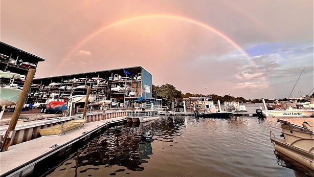 Ein Yachthafen mit vertäuten Booten, ein überdachtes Gebäude und ein Regenbogen am Himmel.