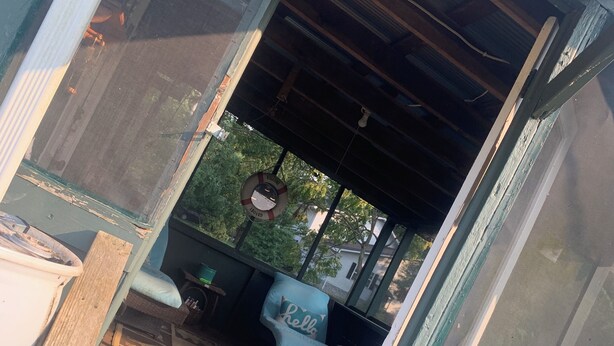 Un espacio al aire libre cubierto con un banco de madera y una silla, un cartel de bienvenida y una lámpara colgante.