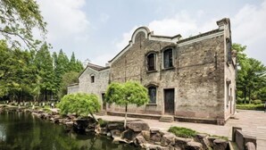 A historic stone building with a pond and trees in front.