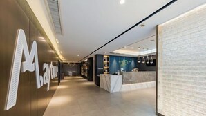 A modern hotel lobby with a reception desk, a large 'M' logo on the wall, and a reception area with a blue accent wall and pendant lights.