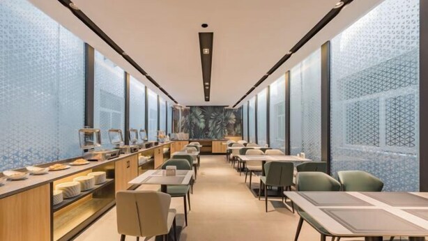 A modern restaurant with long tables and chairs, a counter with food items, and patterned walls.
