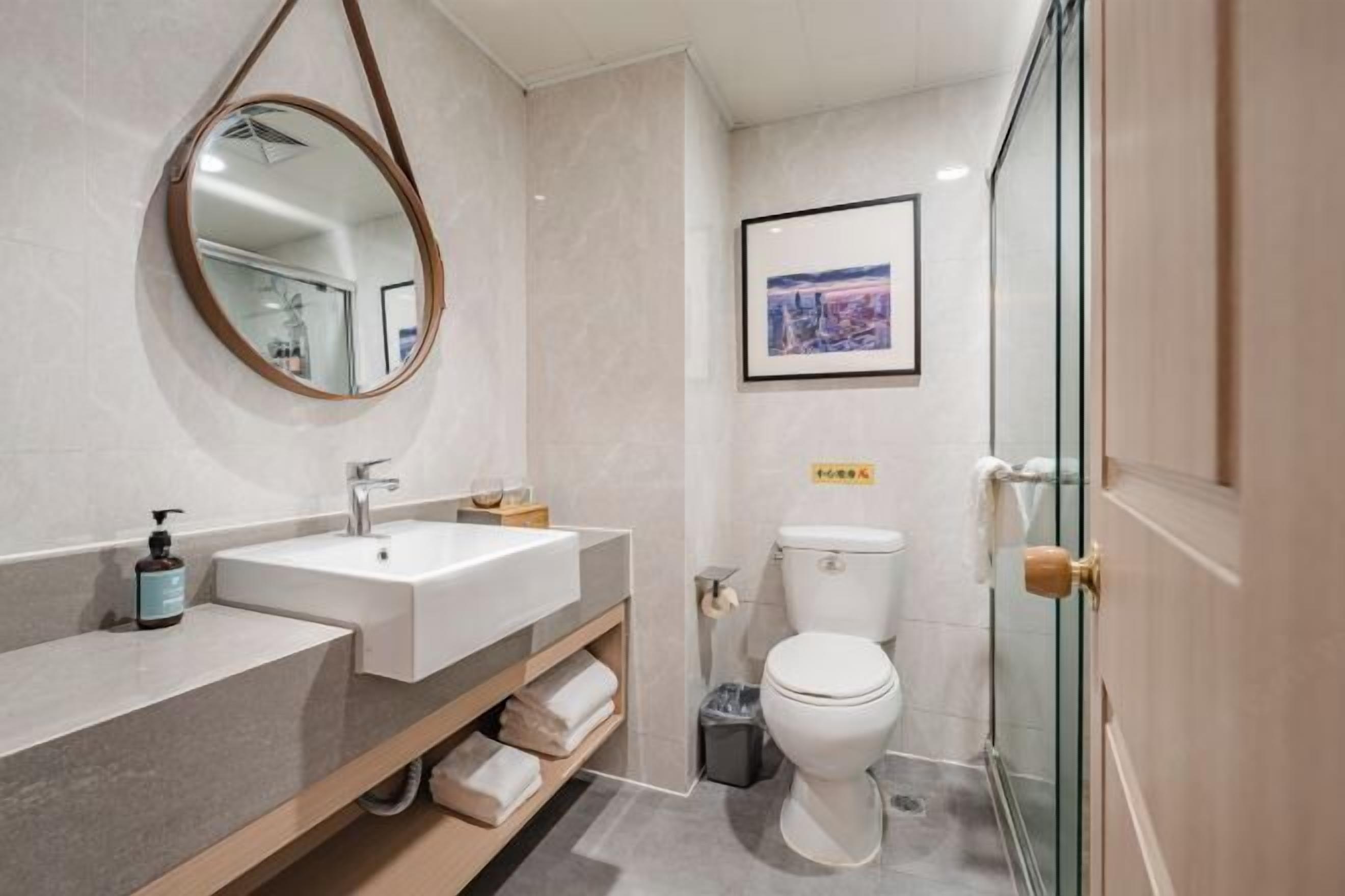 A modern bathroom with a round mirror, two sinks, a toilet, and a glass shower enclosure.