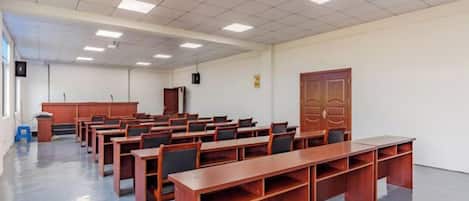 Une salle de conférence avec des rangées de tables et de chaises en bois, un pupitre et une grande porte en bois.